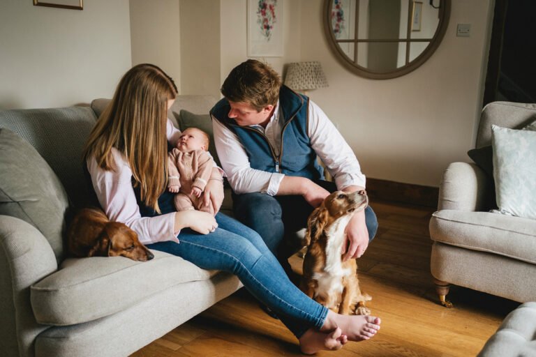 A couple with their newborn baby and two dogs sitting together at home during a baby photo session in Somerset