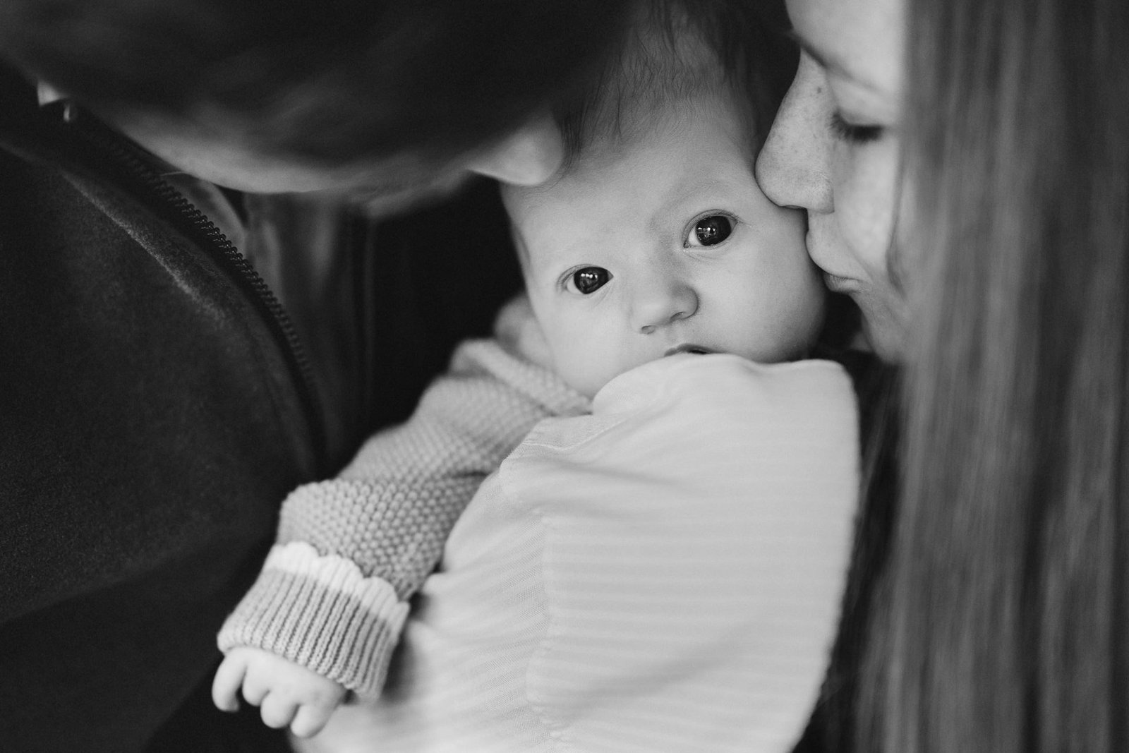 A close up black & white image from a Somerset photography session of two parents kissing a new baby