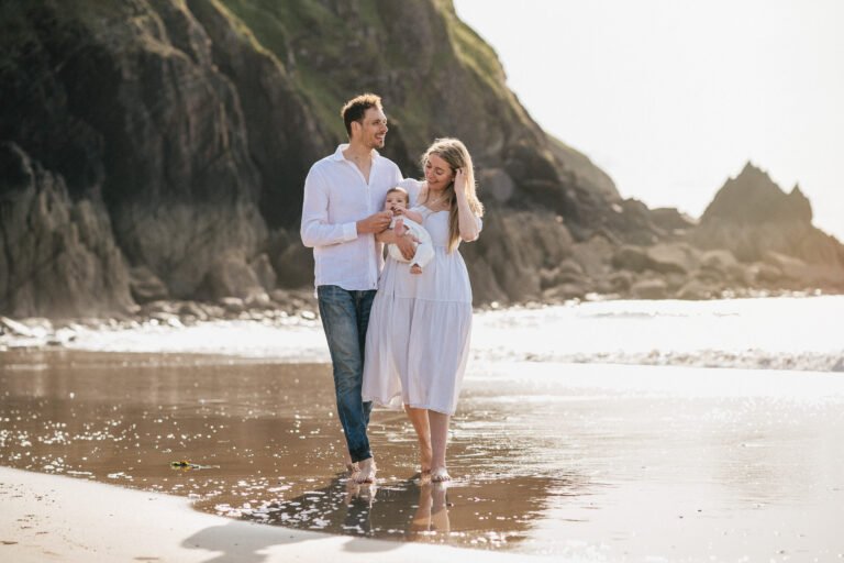 Parents with a baby walking on the beach at sunset during a baby photography at the beach session