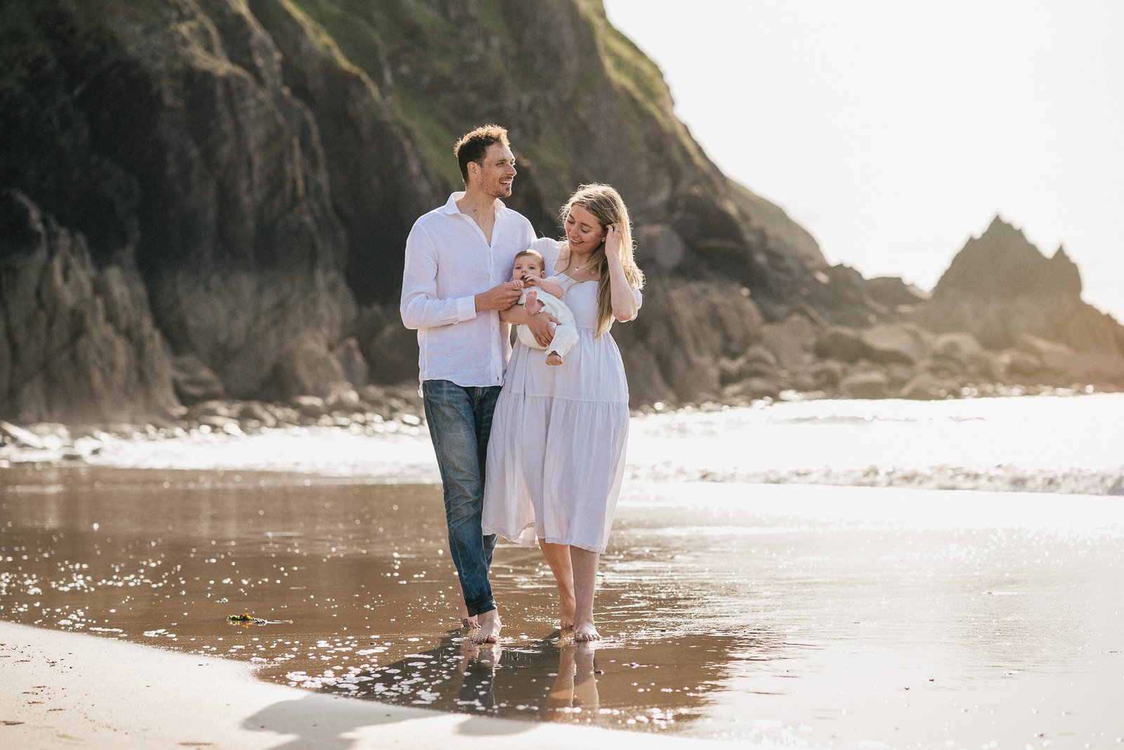 Parents with a baby walking on the beach at sunset during a baby photography at the beach session