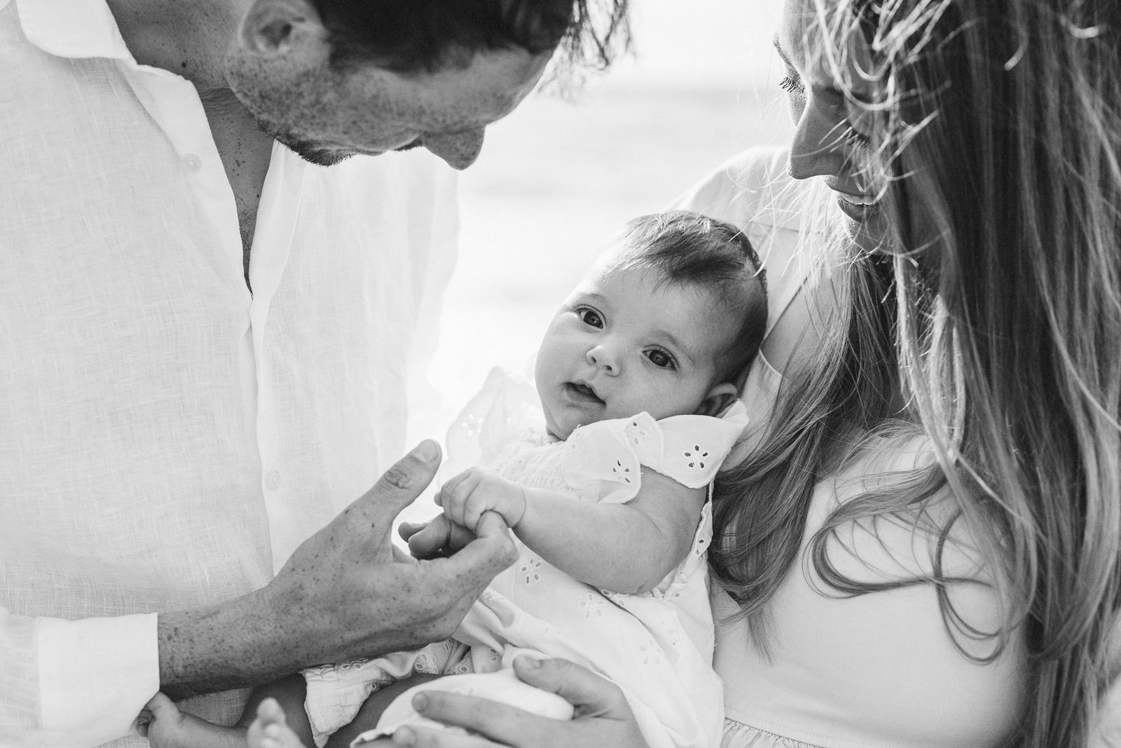 Parents cuddling a young baby during a photography session with the sea behind them