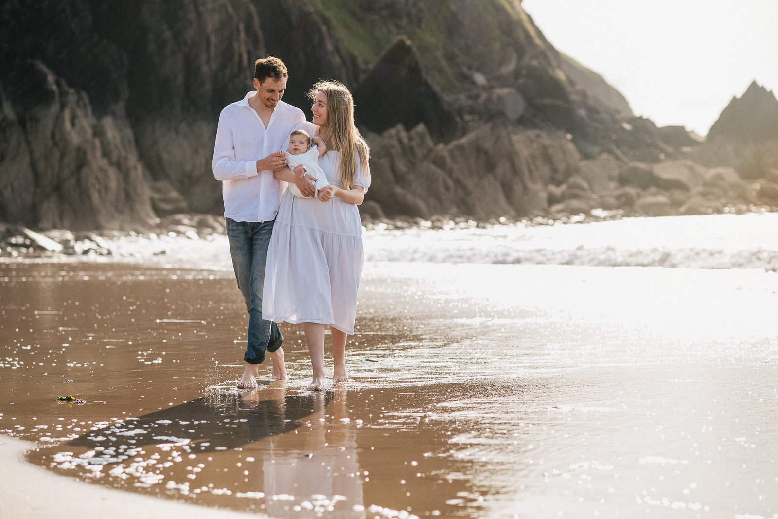 Parents with a young baby walking along the beach during a baby photo session by the sea