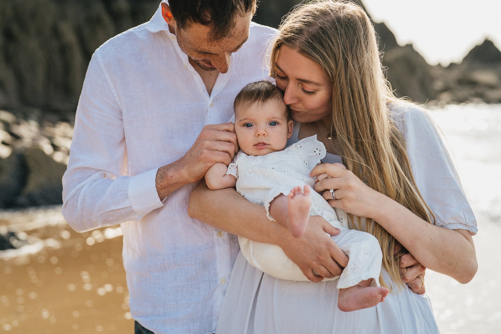 Parents cuddling a young baby during a photography session on the beach in Devon